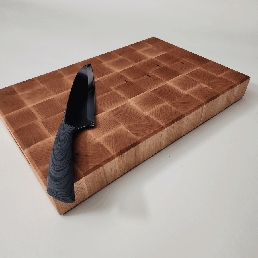 Angled view of 2 inch maple cutting board with knife on top for perspective