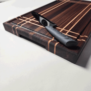 Side view of walnut and maple stripe cutting board showing bottom finger grips.