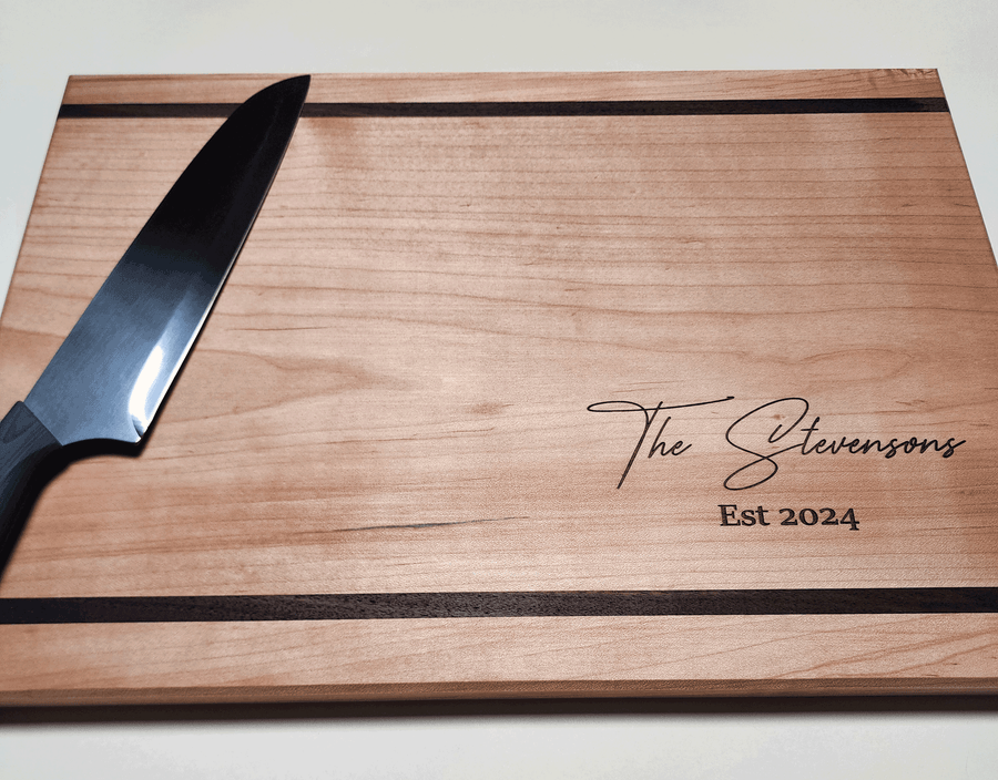 Maple cutting board with Walnut accent lines on top and bottom of cutting board. Custom text engraved in bottom right corner of cutting board.